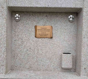 Lápida de piedra con fondo de piedra y placa de metal color oxido con letras negras